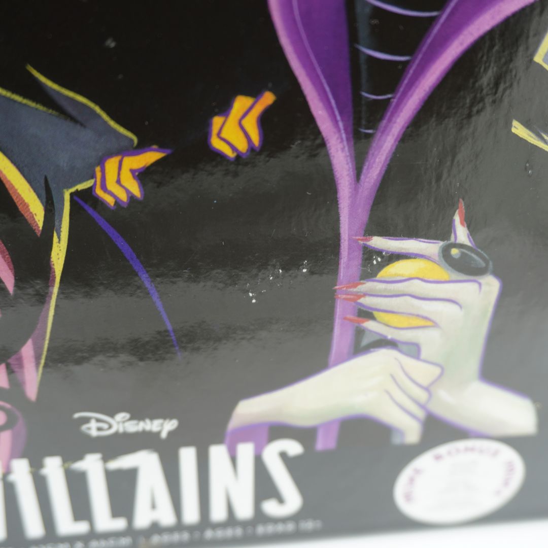 Close-up of a Disney Villains collectible figure or art print featuring a white skeletal hand holding a yellow orb, with purple and black background elements and the Disney Villains title visible.