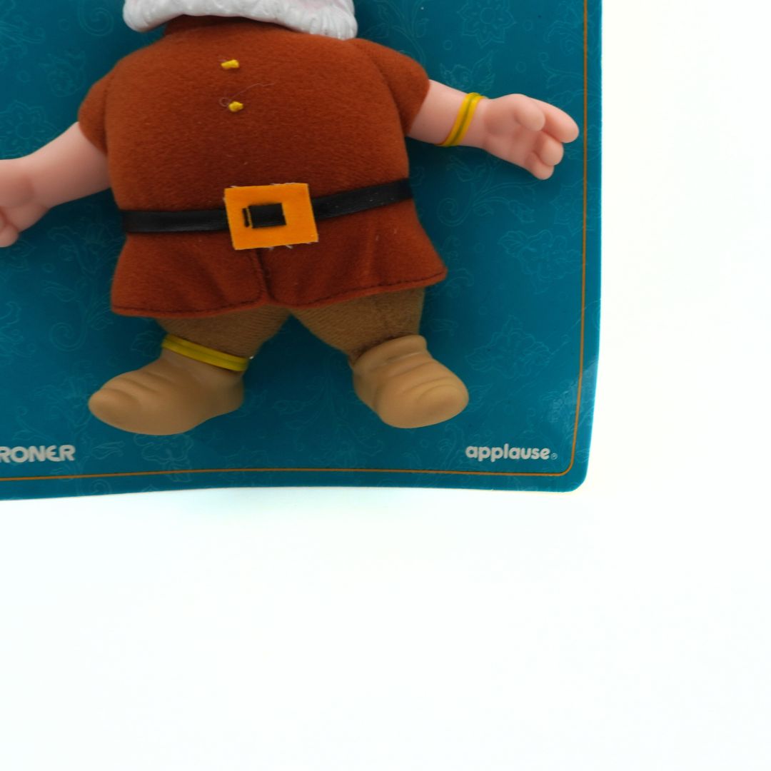 Toy figure of a character in brown outfit with orange buckle on a blue mat with 'Applause' branding.