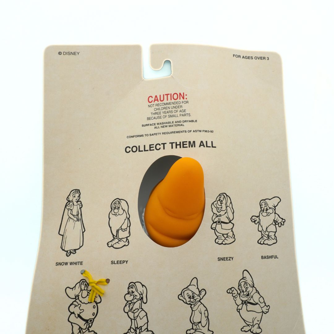 Toy figure in packaging with character illustrations and safety warning on beige background