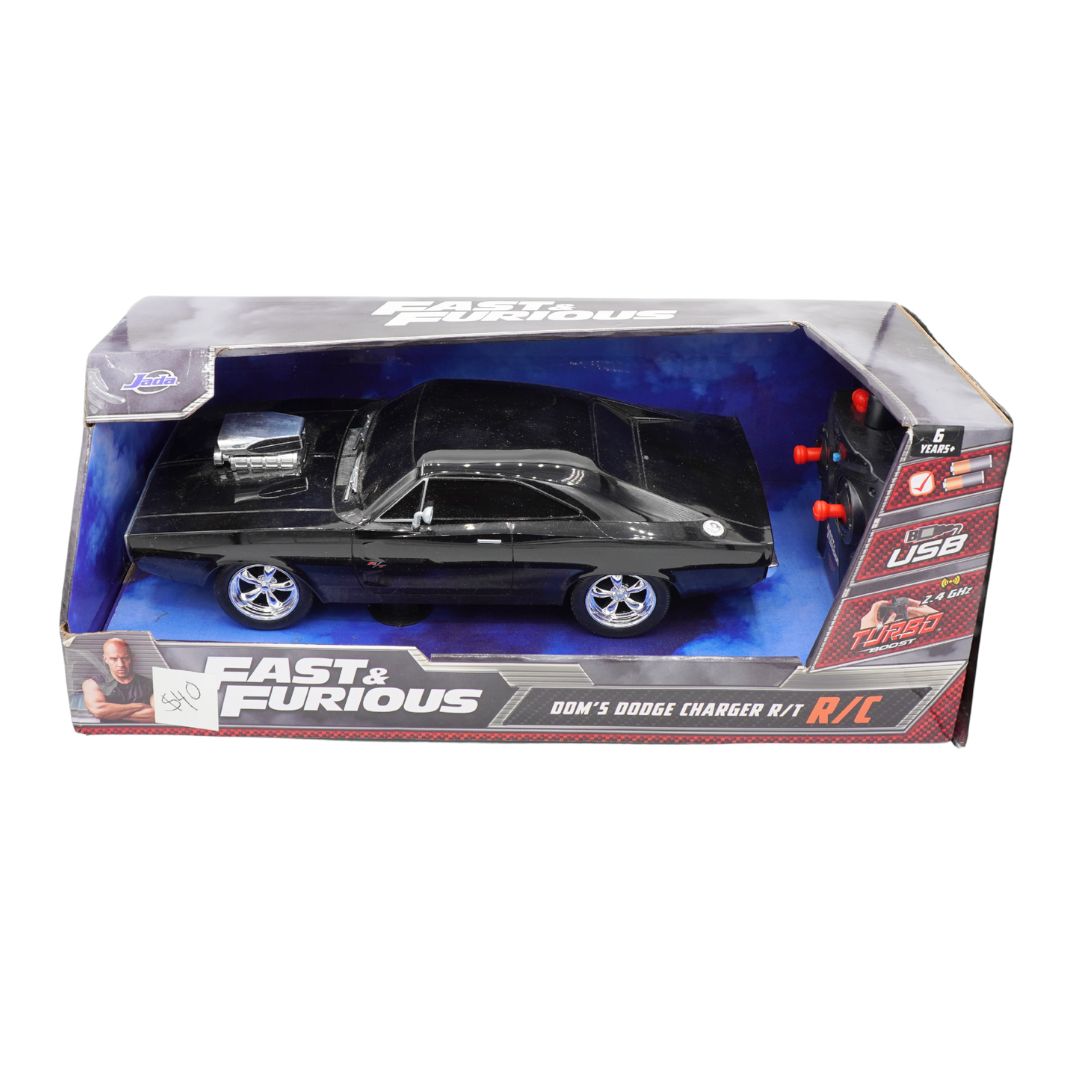 A boxed Fast & Furious Dom's Dodge Charger R/T RC toy car set on a plain white background. The retail package contains a black die-cast model car with chrome wheels and visible engine details, plus a small remote control with red buttons.