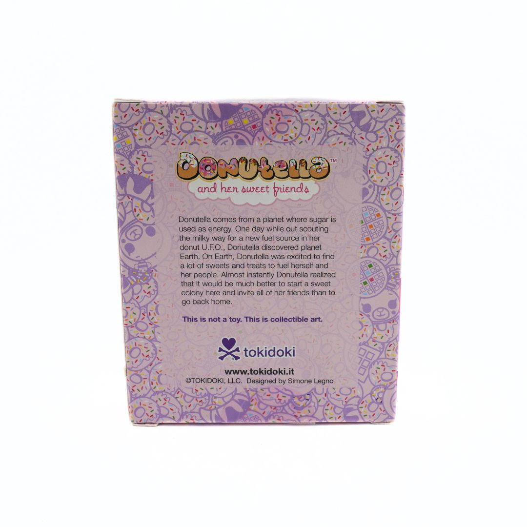 The back of a square collectible art box for 'Donutella and her sweet friends' by tokidoki, featuring a light purple background with a pink and yellow floral pattern and product details printed in black.