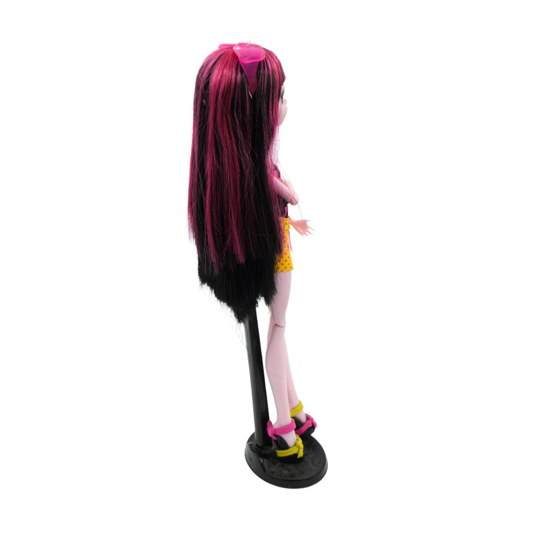 Side on photo of a 2010 Monster High Draculaura from the Gloom Beach range wearing a black shirt and yellow skirt, photographed on a black stand on a white background