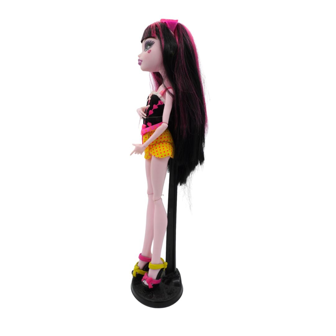 Front on photo of a 2010 Monster High Draculaura from the Gloom Beach range wearing a black shirt and yellow skirt, photographed on a black stand on a white background
