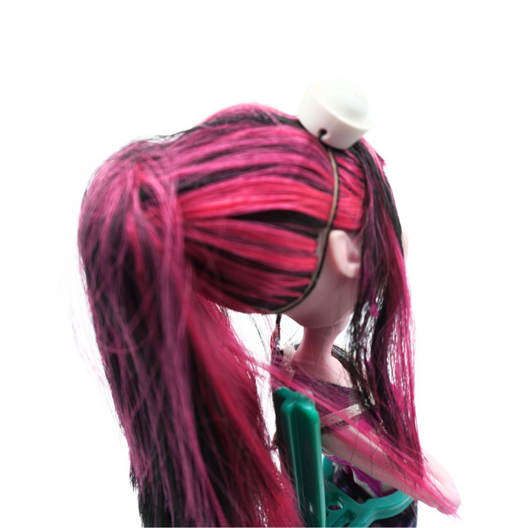A close-up side view of a doll or character with long, messy pink and black hair, wearing a white hair clip, against a plain white background.