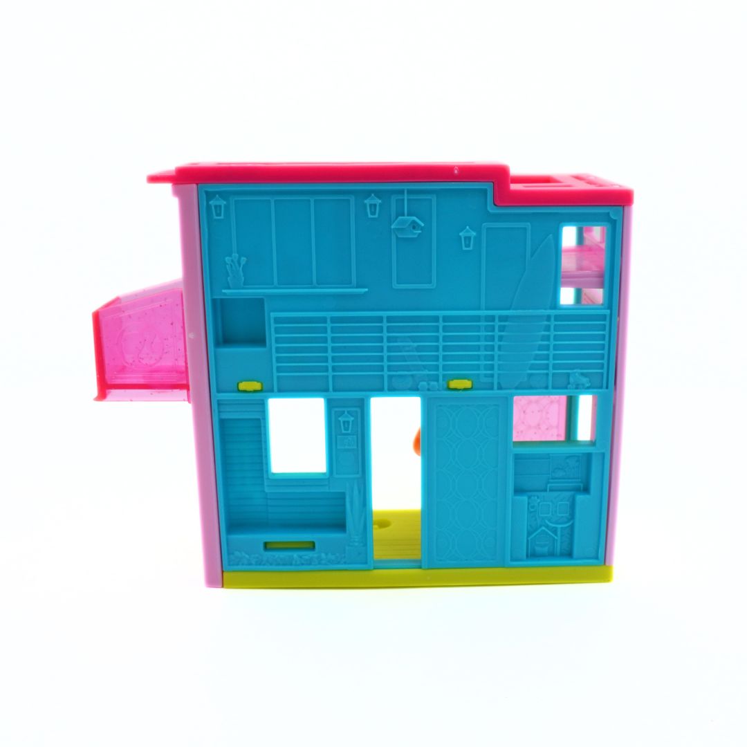 A colorful plastic toy house dollhouse with a bright blue body, pink roof and side extension, yellow base, and small green details, shown on a plain white background.