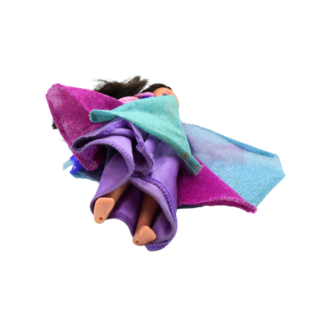 A doll wrapped in a colorful glittery blanket featuring purple, teal, and blue sections, isolated on a white background.