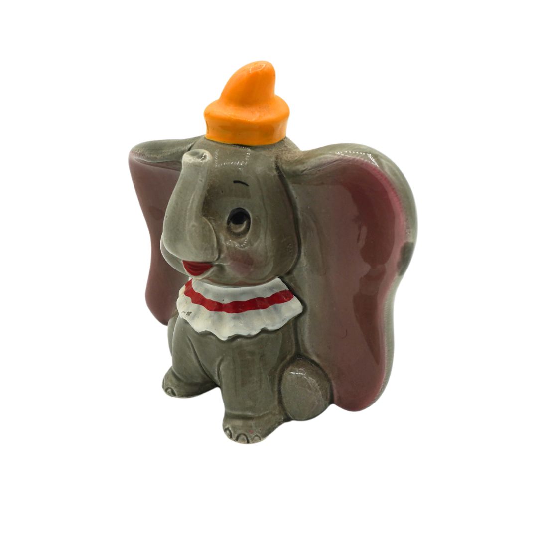 A small Dumbo the Elephant figurine, featuring a gray body, large reddish-brown ears, an orange hat, and a white ruffled collar with a red stripe, set against a plain white background.