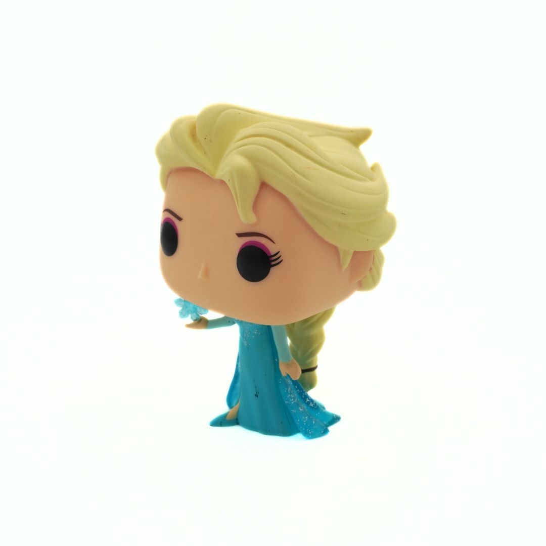 Toy figure of a character with blonde hair and a blue dress on a white background