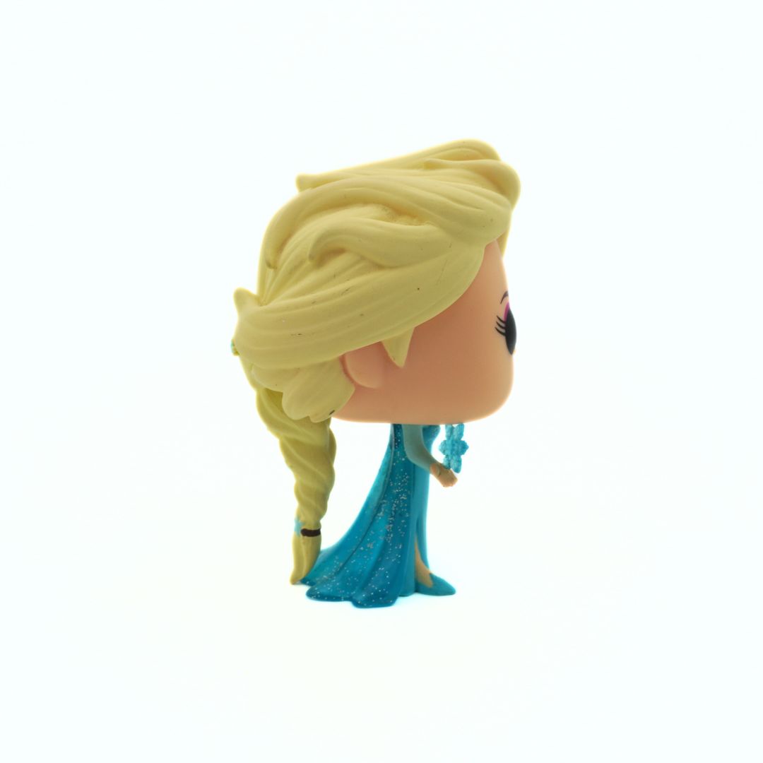 Toy figure of a character with blonde hair and a blue dress on a white background