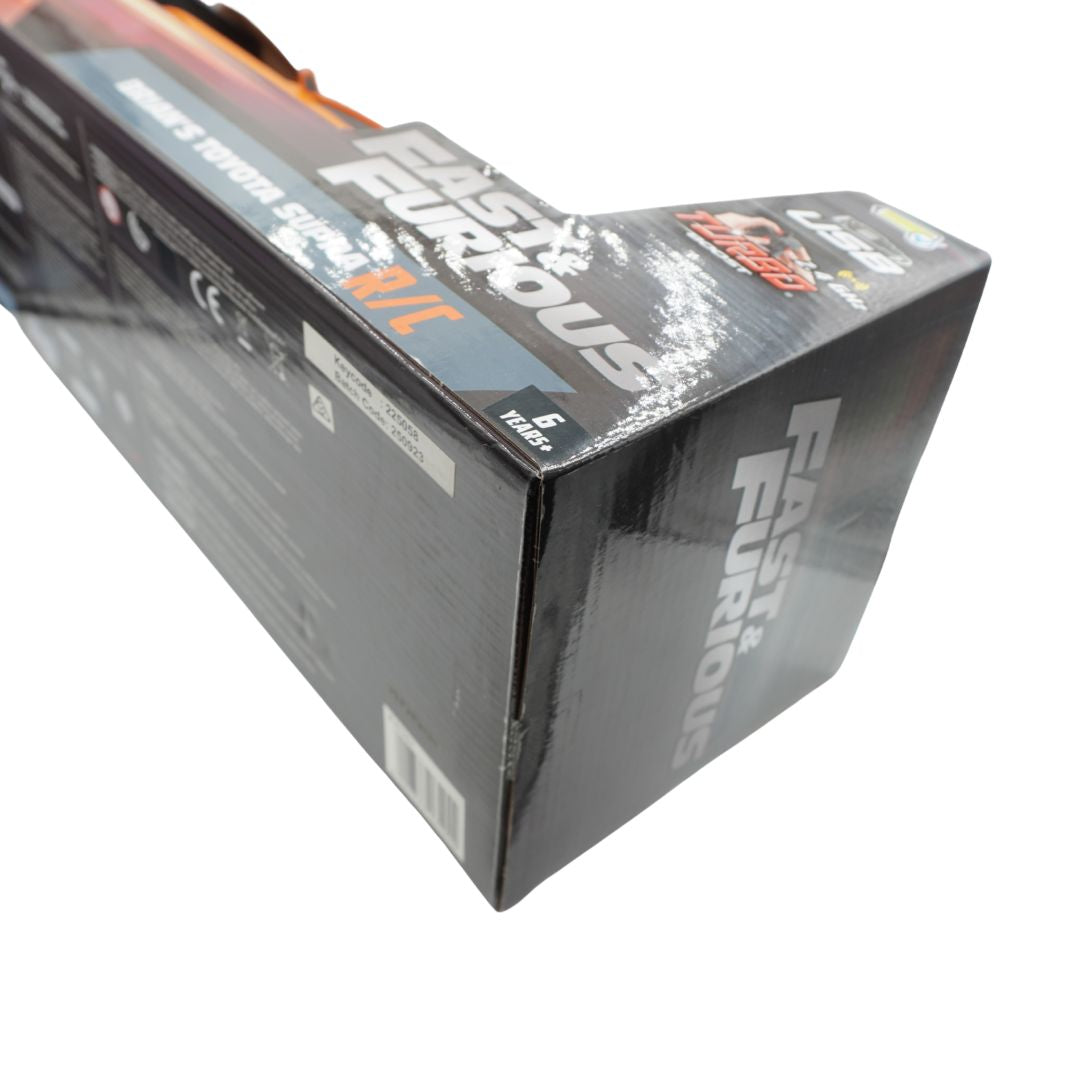 A long rectangular product box for Fast & Furious, photographed at an angle on a plain white background. The box is predominantly black with large white and orange branding and some blue accents.