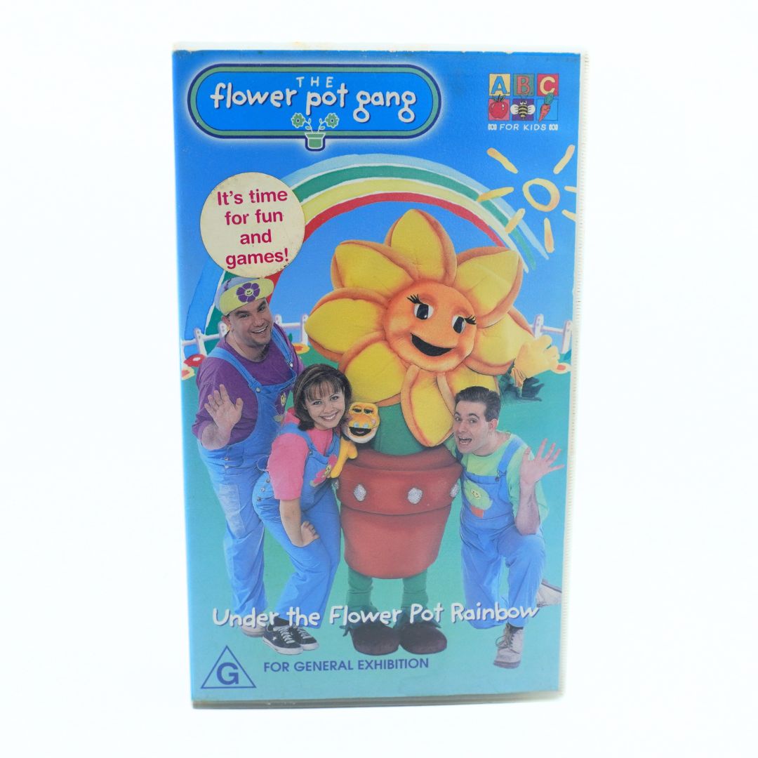 A vintage VHS video case for 'The Flower Pot Gang' children's show, titled 'Under the Flower Pot Rainbow'. The cover features a bright blue background with a large smiling yellow flower pot character, two children in colorful outfits, and two adults.