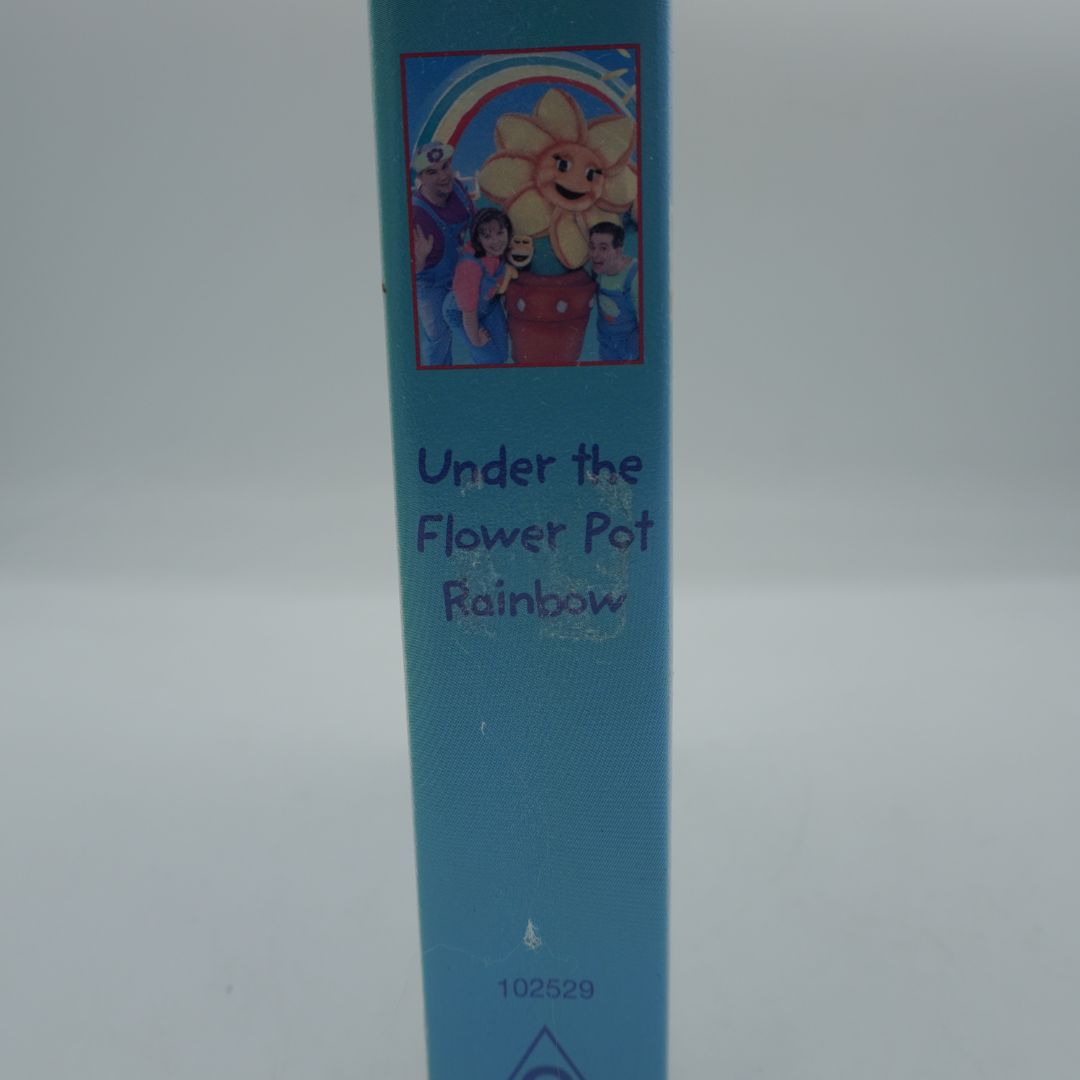 A close-up of a children's book spine titled 'Under the Flower Pot Rainbow' in purple text on a light blue background, with a small colorful illustration of a flower pot and children near a rainbow at the top.