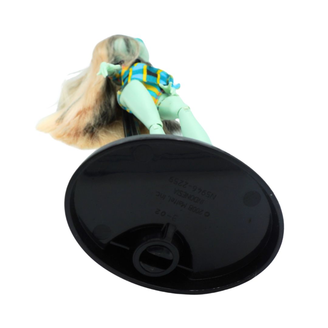 A vintage-style doll with long blonde hair, wearing a blue and yellow striped top and mint green pants, attached to a large black oval base. The doll is photographed against a plain white background.