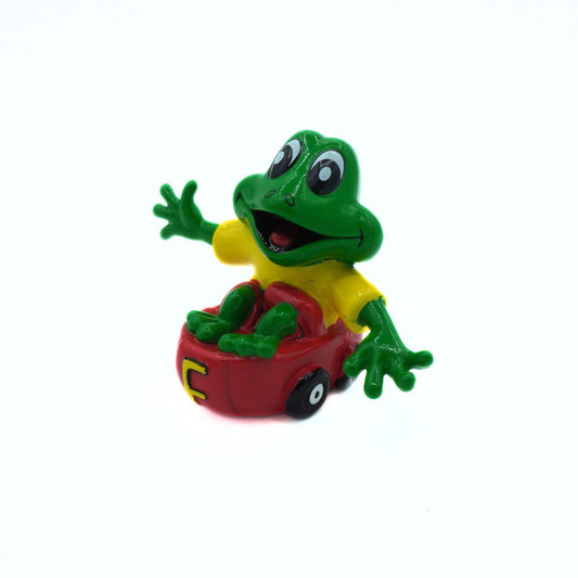 Toy frog in a red car on a white background