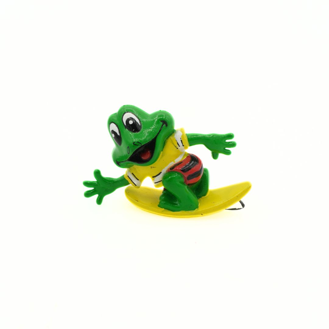 Toy frog on a yellow surfboard with a white background