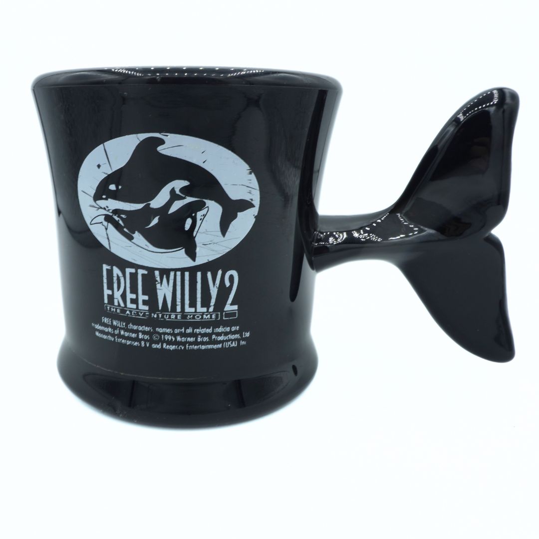 Black mug with fish-shaped handle featuring 'Free Willy 2' logo on a white background