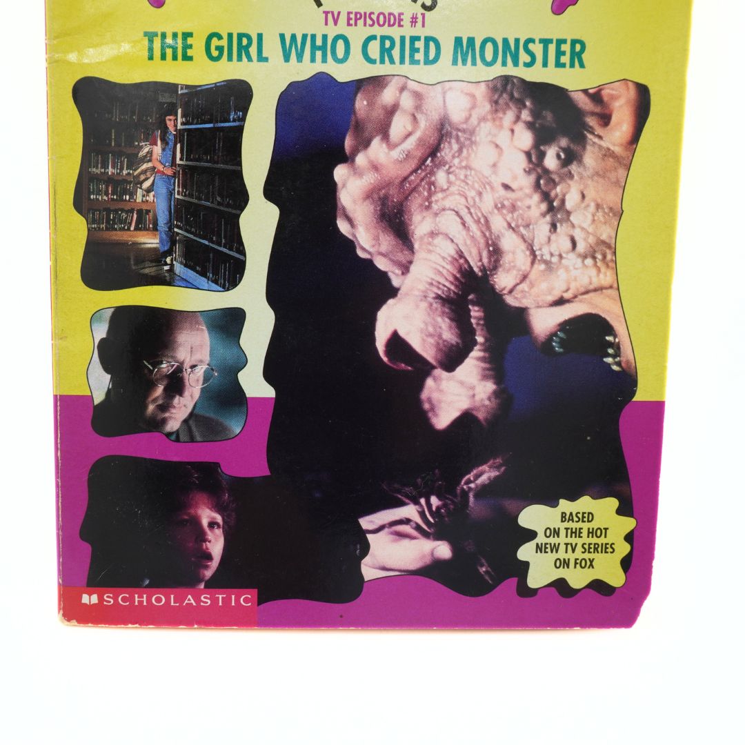 Book cover of 'The Girl Who Cried Monster' by Scholastic with images and text on a yellow and pink background.
