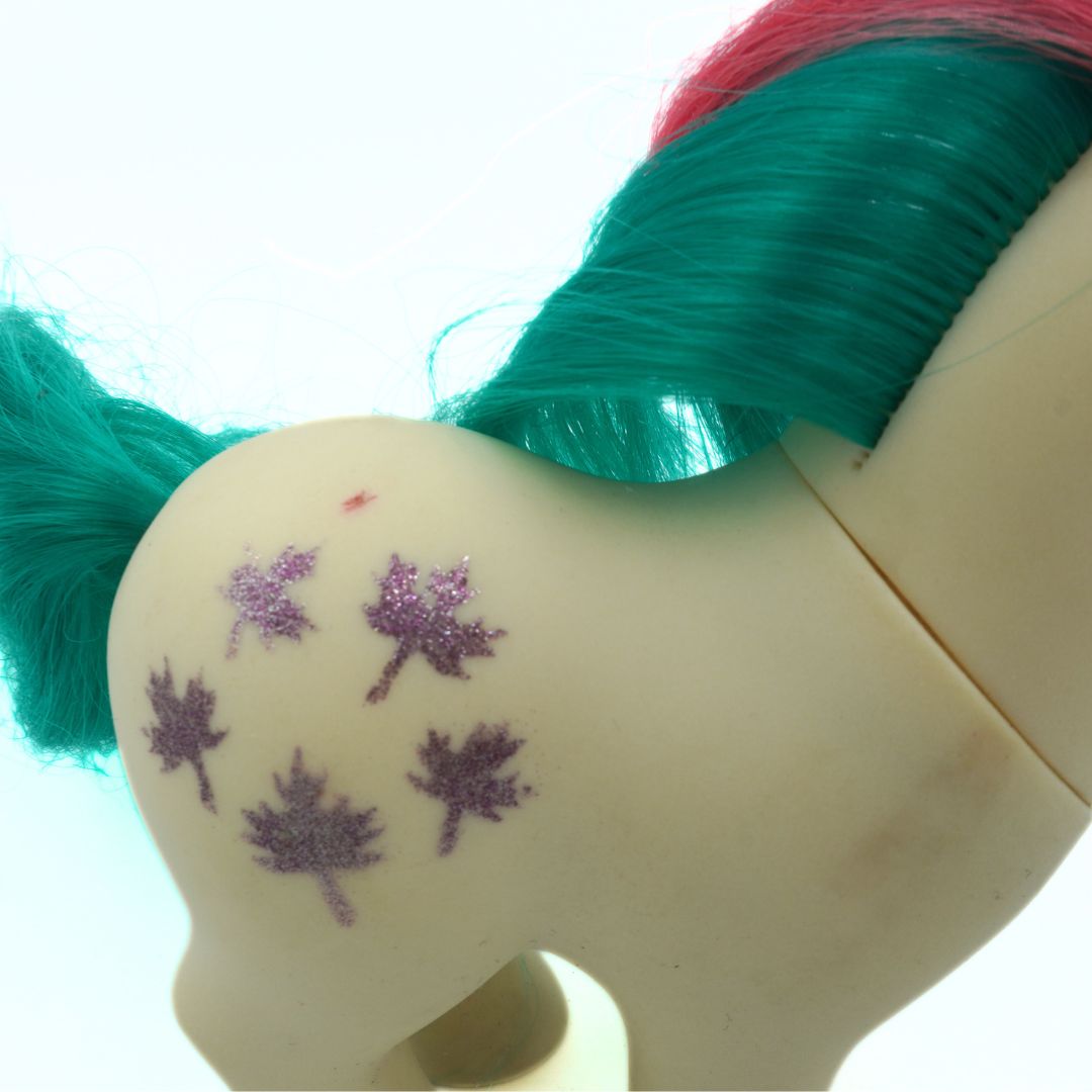 Close-up of a toy figure with teal hair and purple leaf designs on its back.