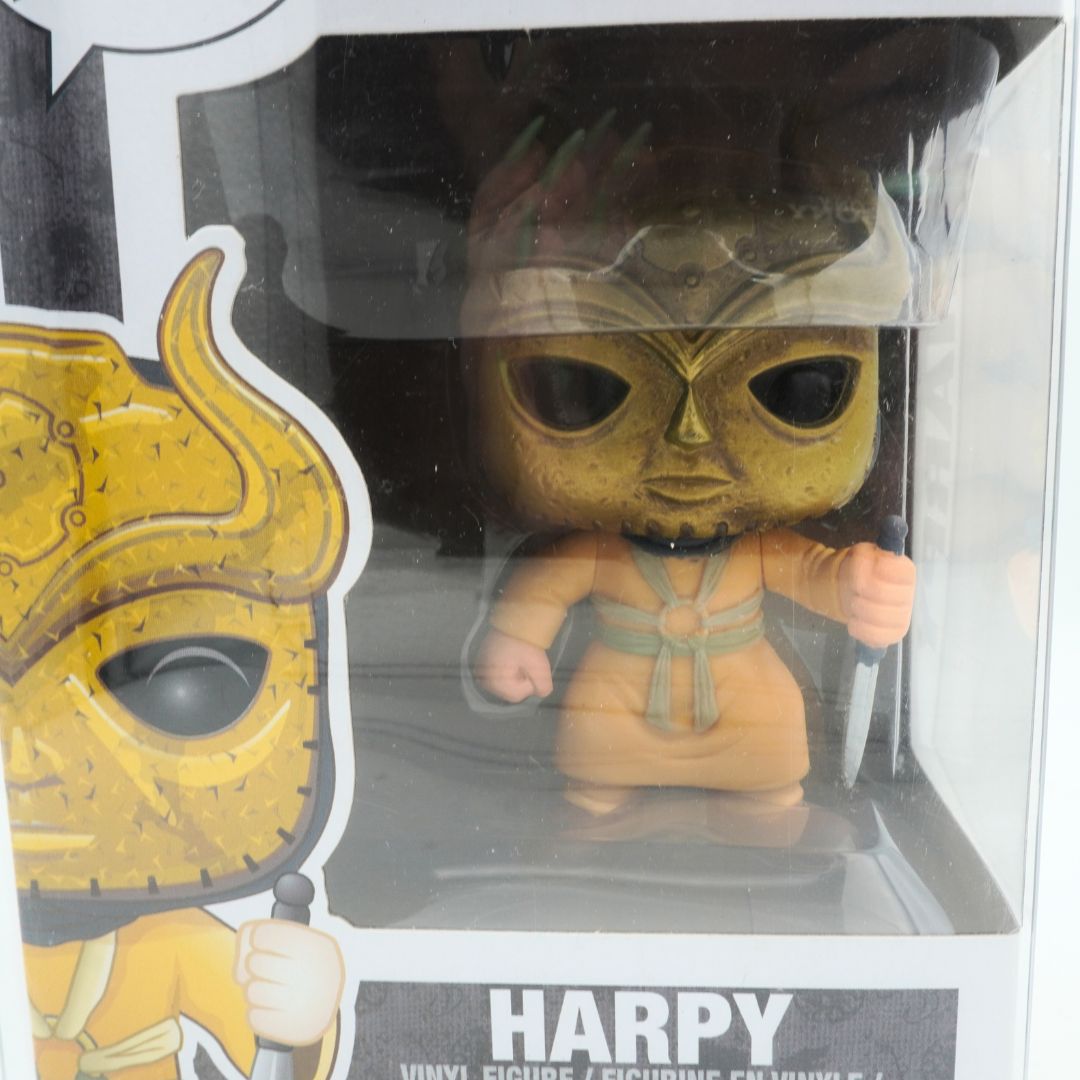 Vinyl figure of a character with gold mask and brown outfit in packaging, character name 'Harpy' visible.