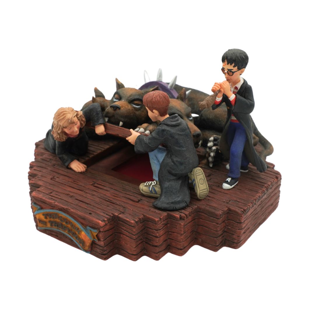 A detailed figurine depicting characters from Harry Potter on a wooden platform, with a large pack of wolves surrounding them. The figures include Harry, Ron, and Hermione in their iconic school uniforms, posed dynamically on a brown wooden-textured base against a plain white background.