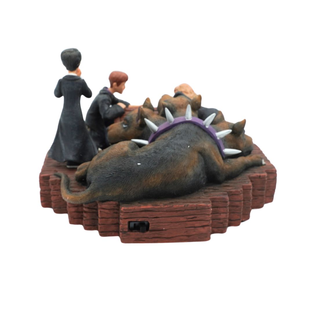 A decorative figurine depicting a man in a black suit and a woman in a long dark dress standing beside a pile of dogs wearing a purple collar with white spikes, all arranged on a reddish-brown pedestal against a plain white background.