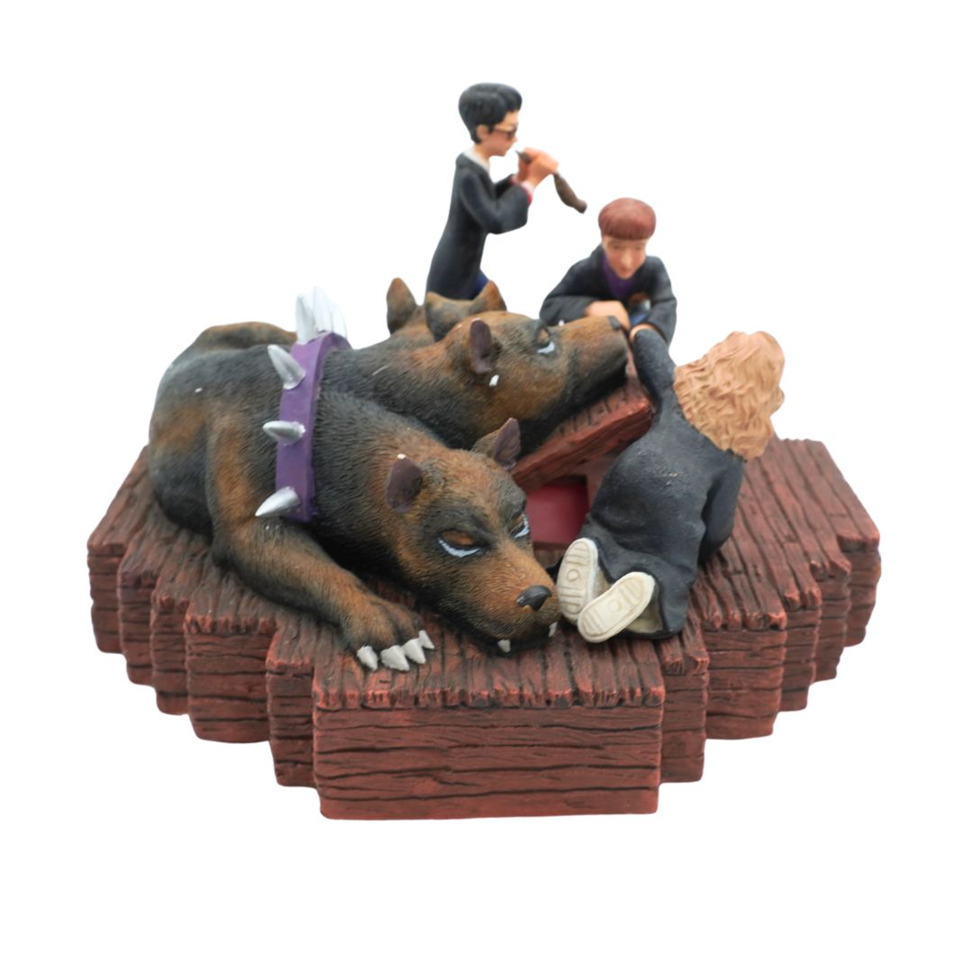 A small figurine depicting two dogs lying on a wooden platform while two people stand and sit nearby, photographed against a plain white background.