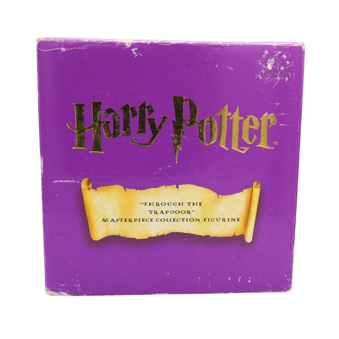 A purple square box for a Harry Potter figure, featuring the Harry Potter logo in black and gold above a yellow scroll graphic that reads 'Through the Trapdoor Masterpiece Collection Figurine.'.