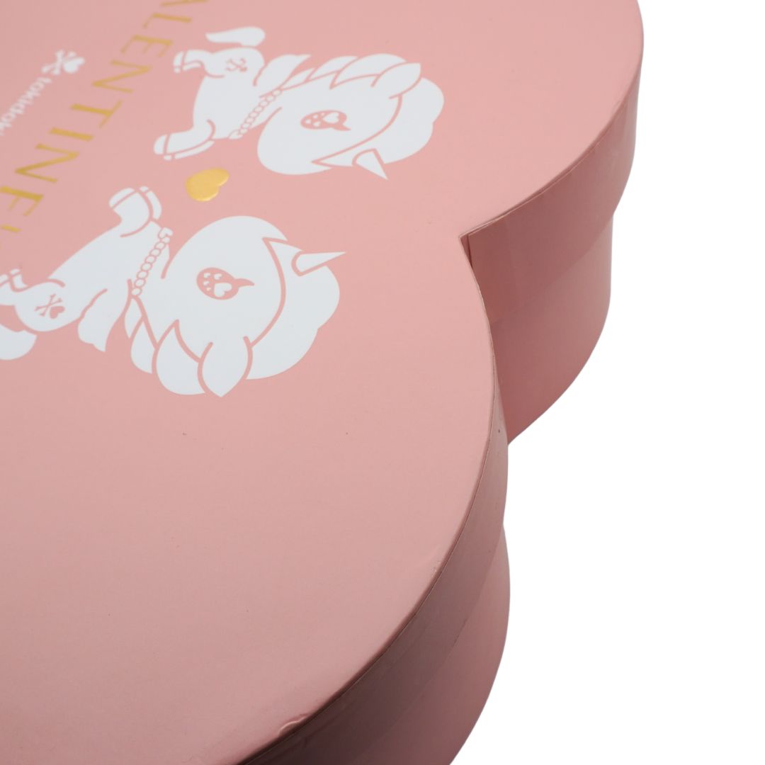 A close-up of a pink heart-shaped gift box lid with white cartoon bunny illustrations and partial gold text reading ' Valentine' on a white background.