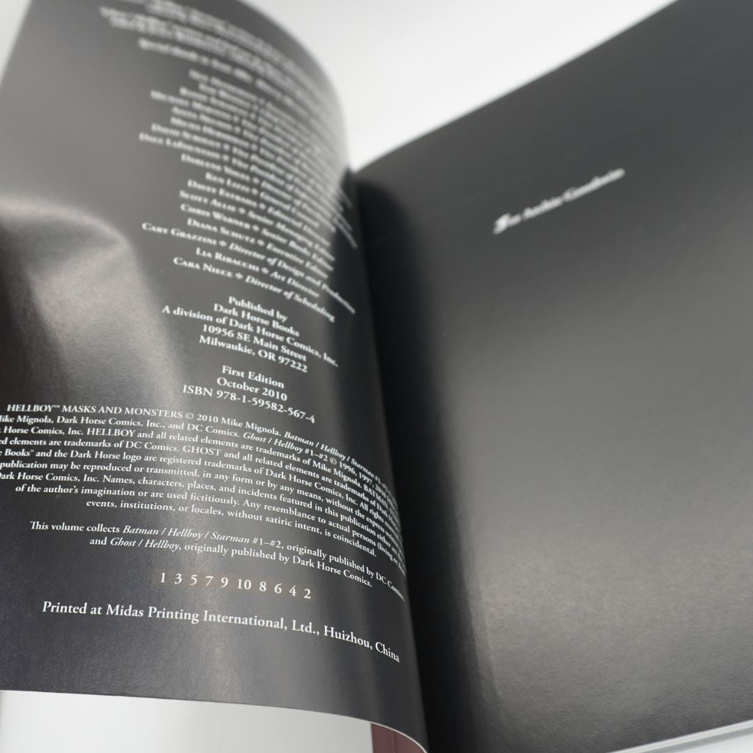 An open book or booklet photographed at an angle, showing printed text on both pages. The right page is dark gray/black, and the left page has white text with publication details.