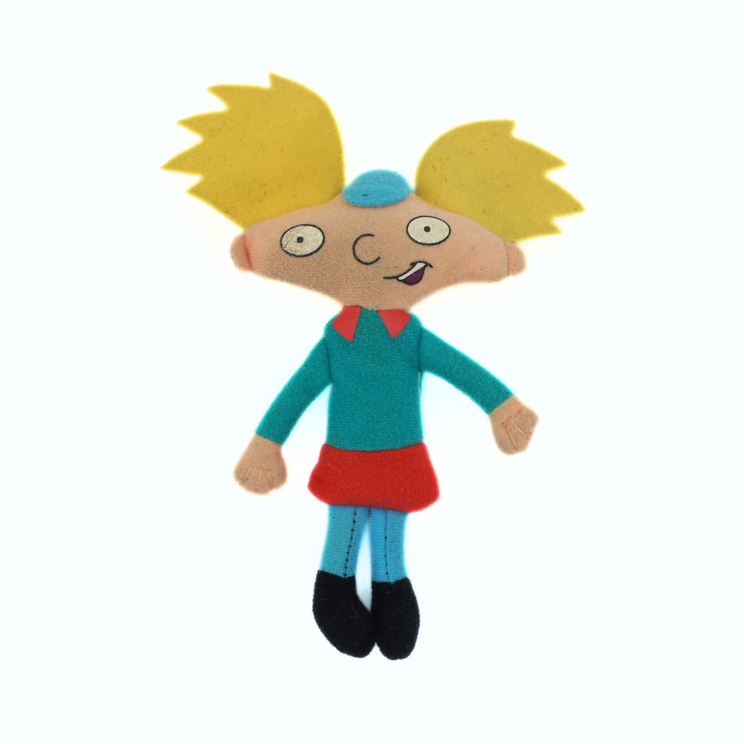 Toy figure with yellow hair, teal shirt, red skirt, and black shoes on a white background