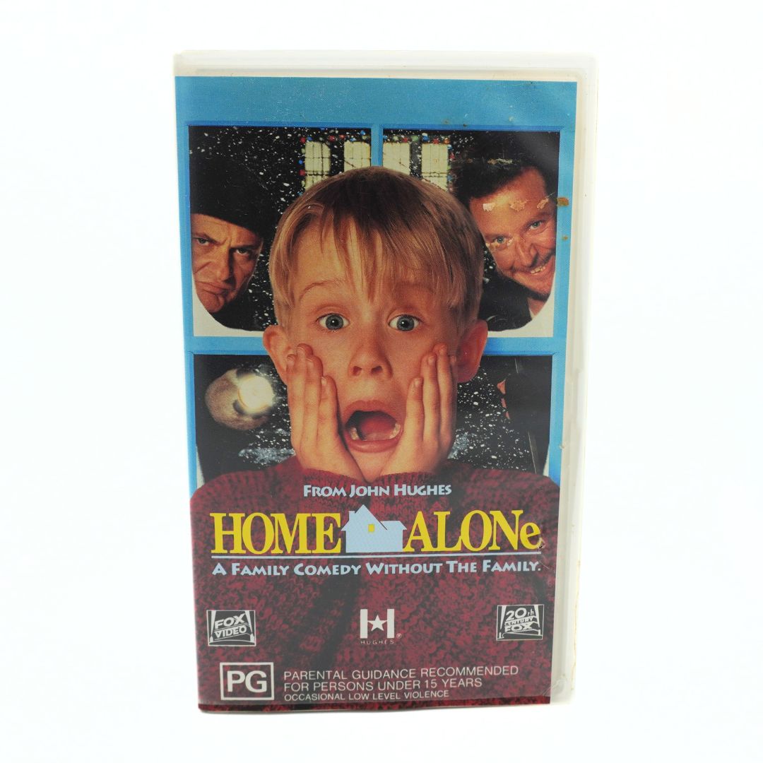 A VHS tape of the movie 'Home Alone' on a plain white background. The cover features a blue border with character photos and the title in yellow and white text.
