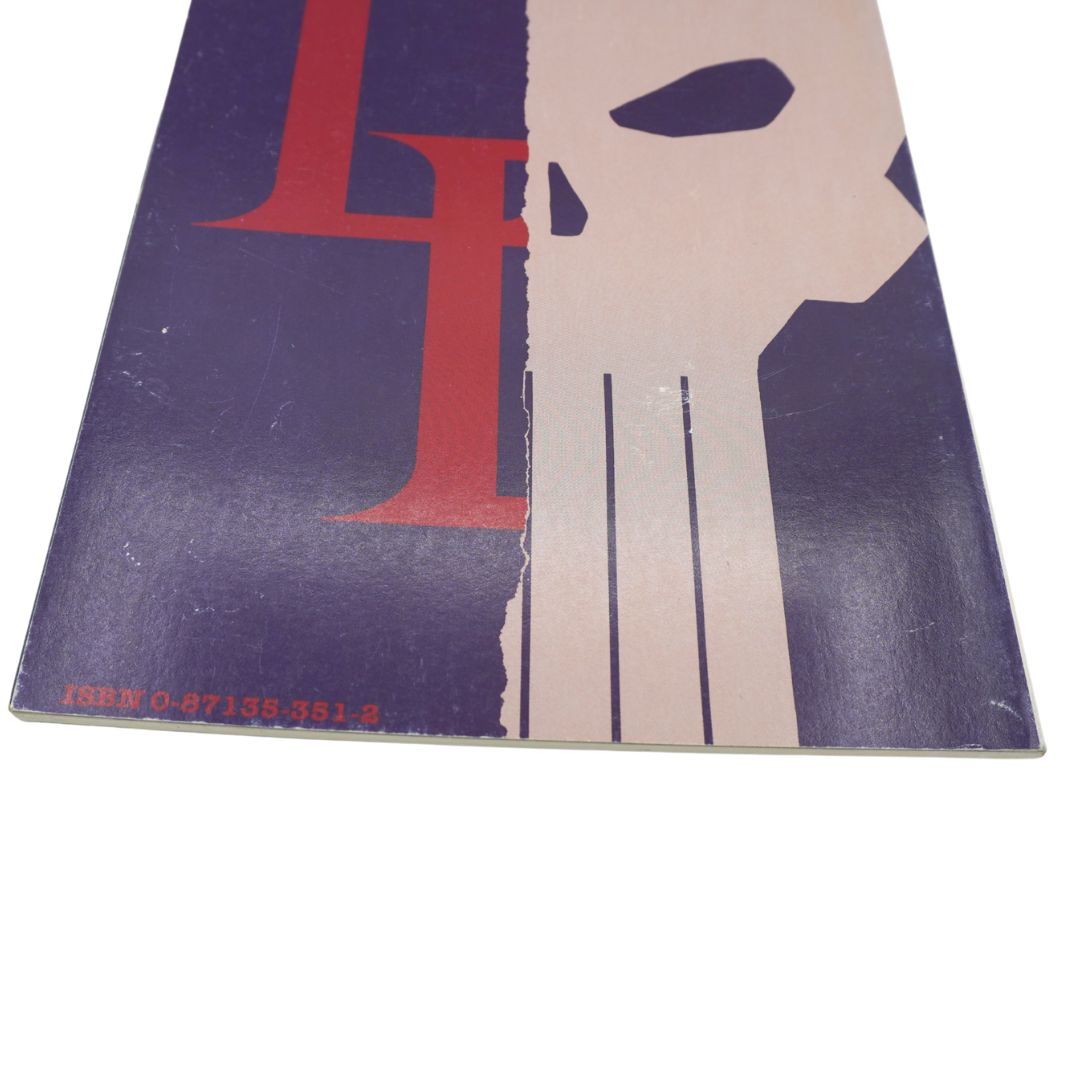 A close-up of a book or magazine cover featuring a stylized graphic split into dark purple, red, and off-white sections, photographed against a white background.