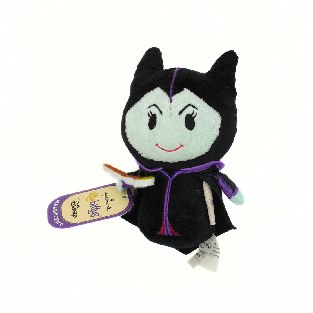 A small plush toy of Disney's Maleficent, featuring her signature black dress, purple trim, and pale blue face, with a hangtag attached.