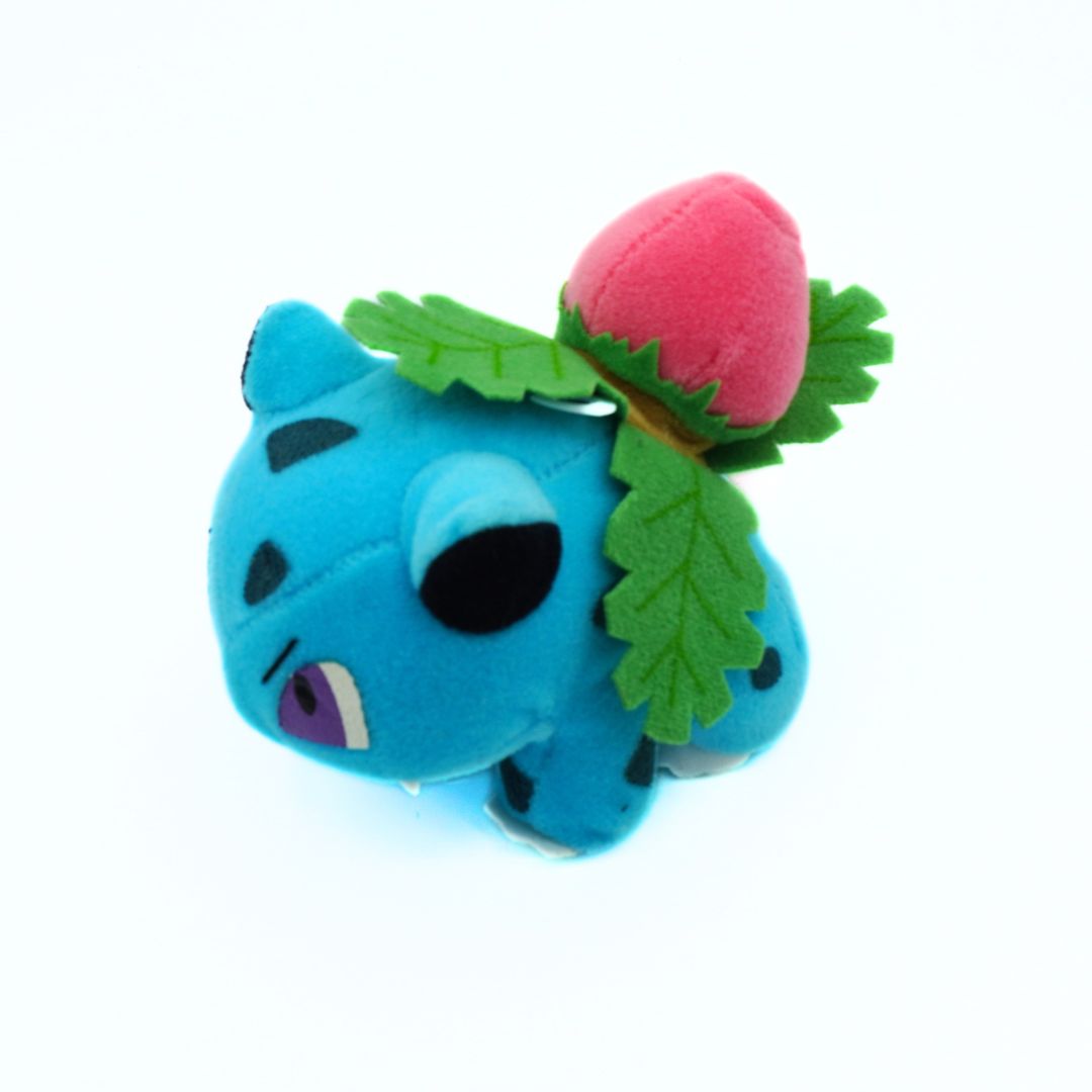 Blue plush toy with a pink ball and green leaves on a white background
