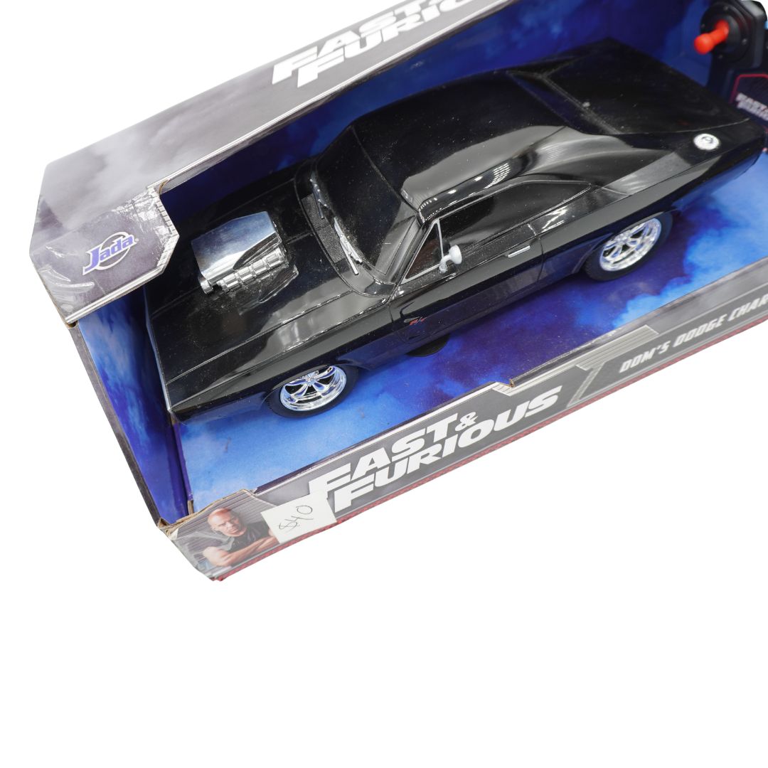 A boxed toy/model car on a plain white background. The product appears to be a black muscle car in retail packaging with visible 'Fast & Furious' branding and a small character photo on the box.