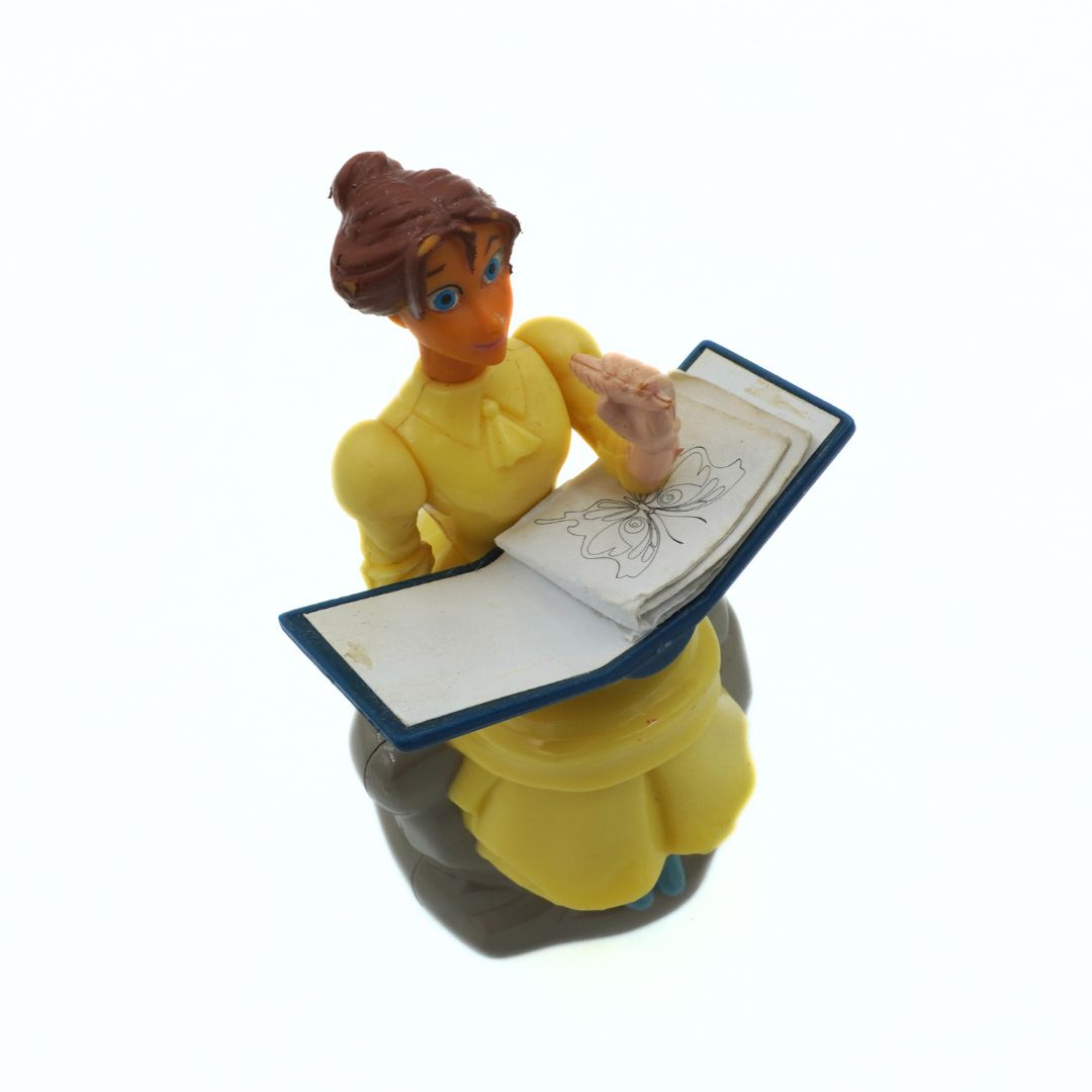 Figurine of a character in a yellow dress holding an open book on a white background