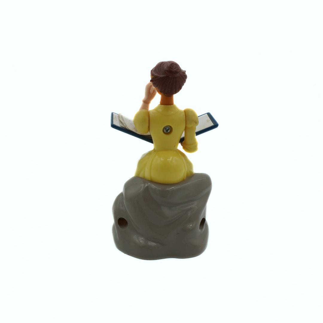 Figurine of a woman in a yellow dress sitting on a rock with a book, on a white background