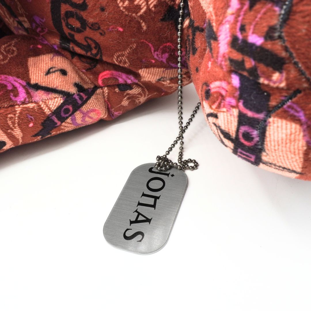 Dog tag necklace with 'Jonas' engraved, placed on a colorful fabric background.