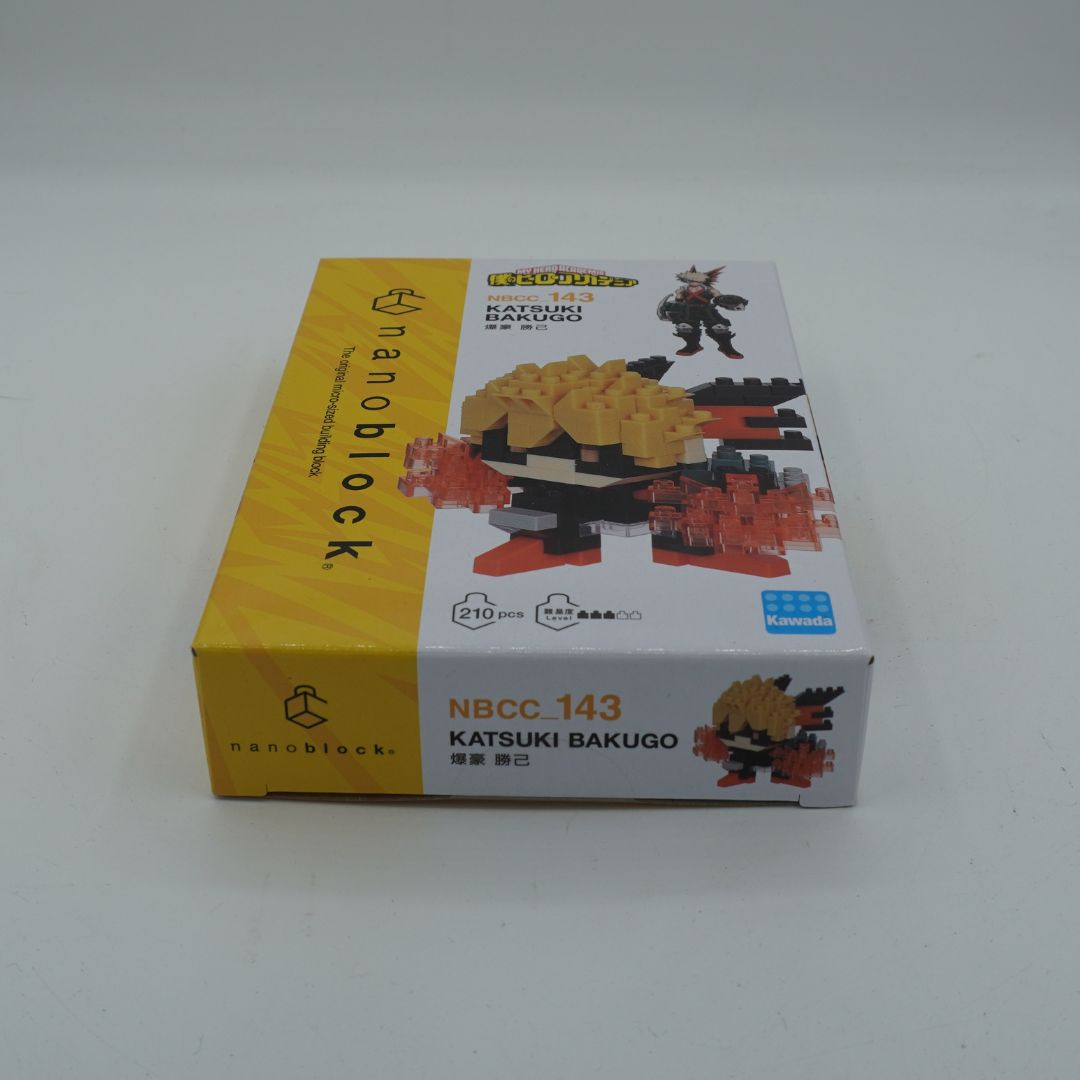 A boxed toy building block set labeled 'nanoblock' and 'NBCC 143 KATSUKI BAKUGO' on a plain light background. The box is mostly white with a yellow side panel and printed images of the assembled toy and character.