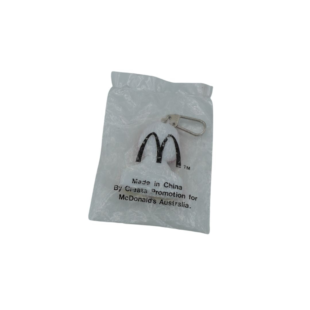 A McDonald's promotional keychain bag in a clear plastic pouch with the golden arches logo and 'Made in China By Quatro Promotions for McDonald's Australia.' printed on it, containing a small white keychain with a silver clasp, shown on a white background.