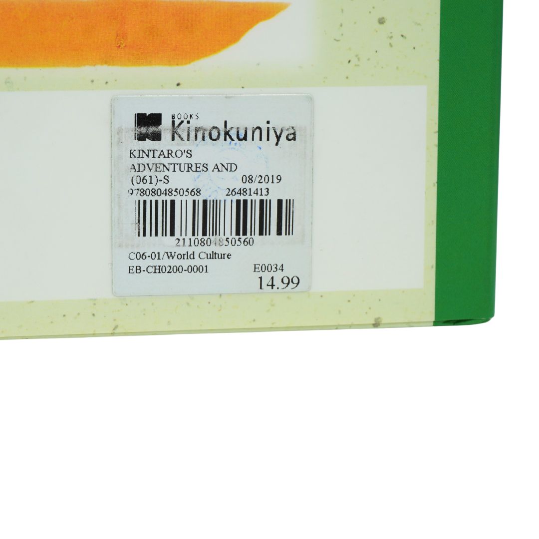 Close-up of a book cover showing the title label 'KINTARO'S ADVENTURES AND (361)-S 08/2019' with barcode, publisher text, and price 14.99 on a mostly white cover with green and orange accents.