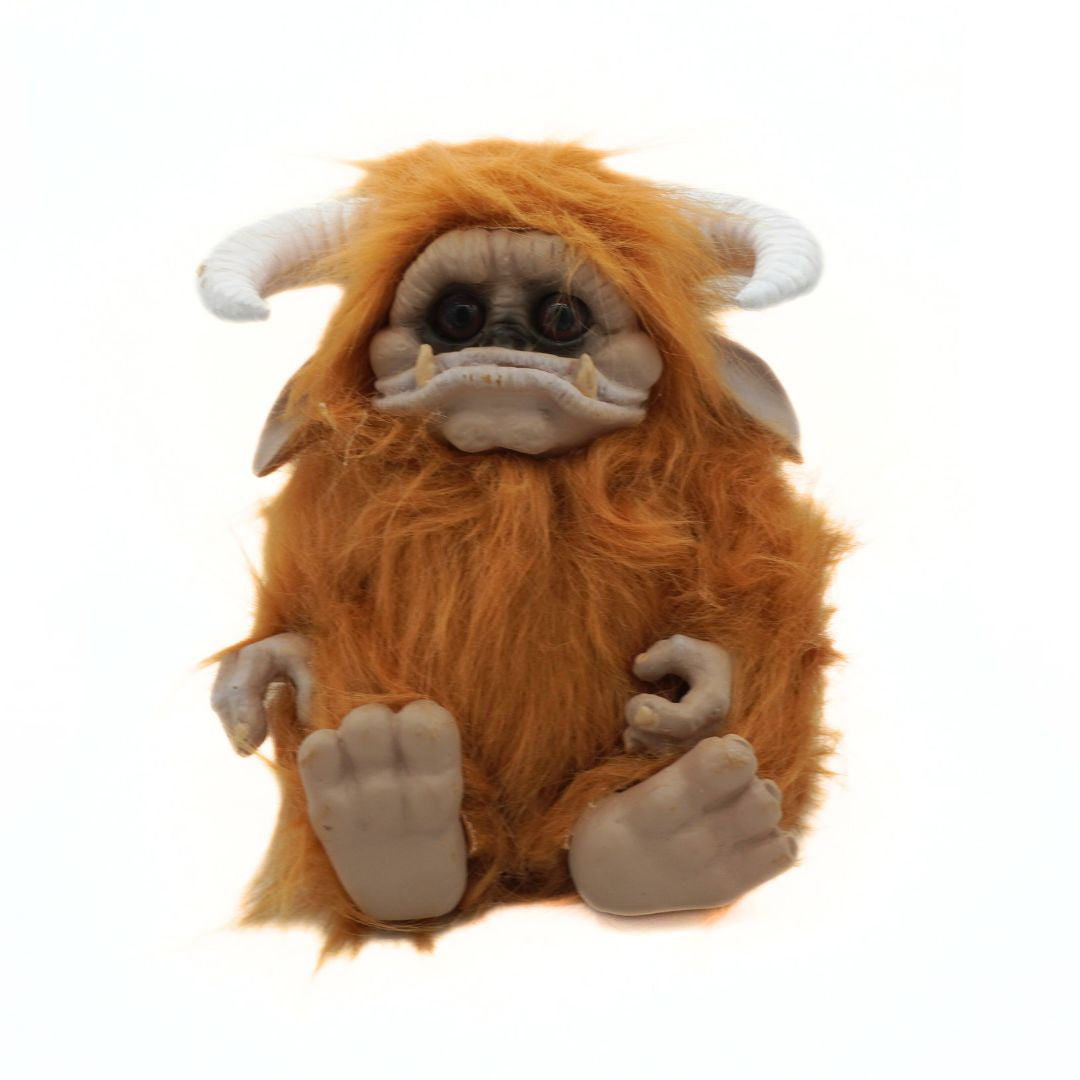Plush toy resembling a creature with orange fur, white horns, and gray hands on a white background