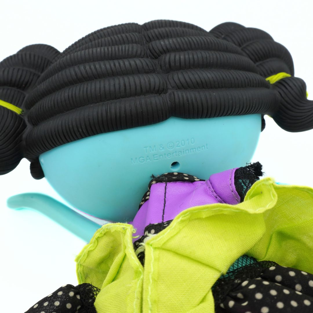 A close-up of a doll with a light blue head, black ribbed hair styled in pigtails, and a bright lime green and purple dress, shown against a white background.