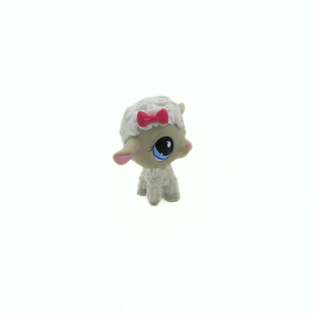 Small toy lamb with a white outfit and pink bow on a white background