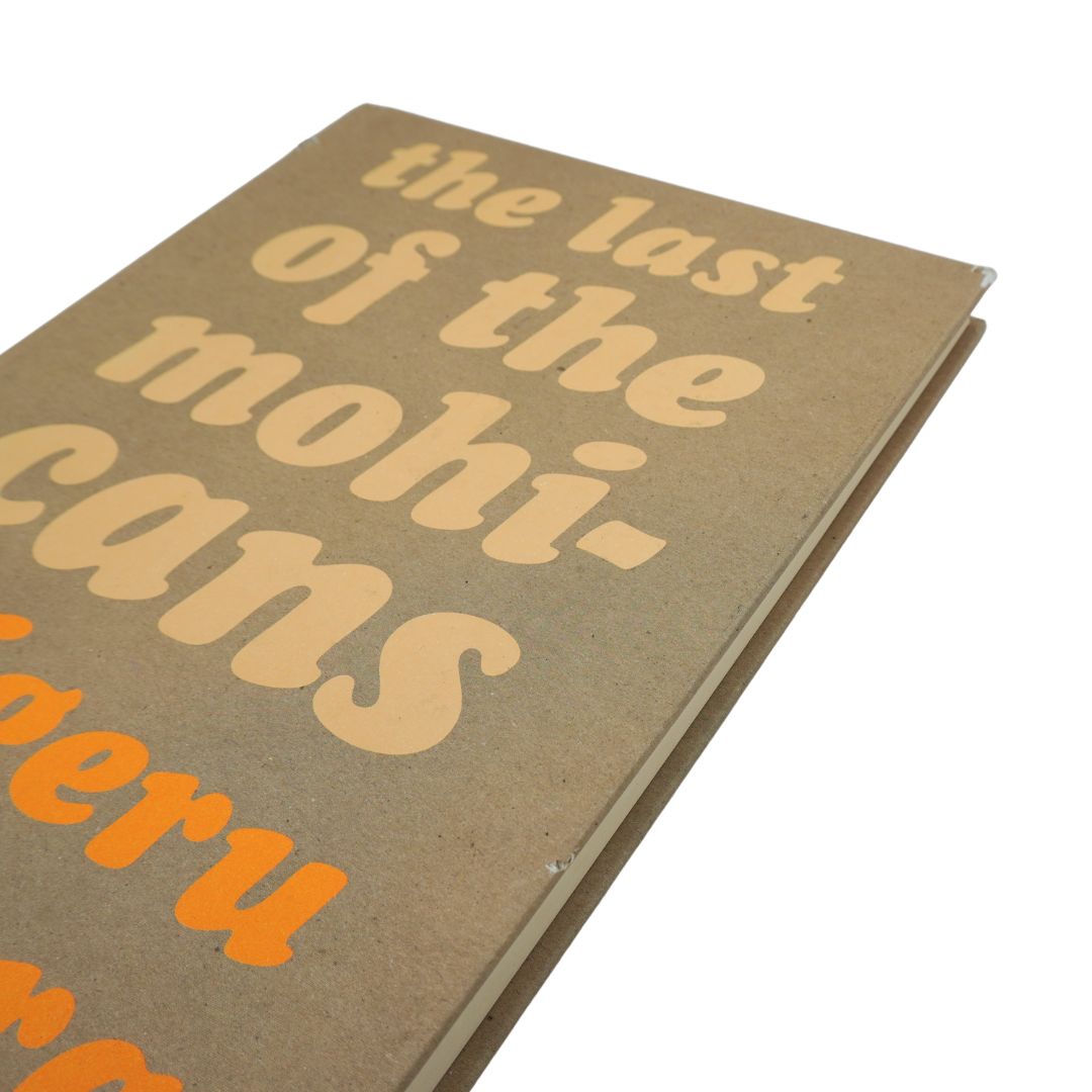A close-up angled shot of a book cover with the title 'the last of the mohicans' in large beige lettering on a brown textured background, with orange text partially visible at the bottom, set against a plain white background.