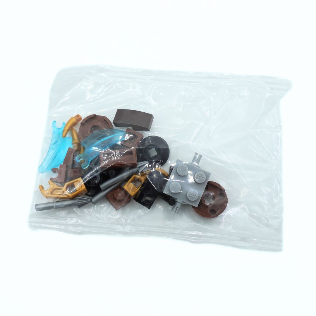 A clear plastic bag containing assorted small toy building block pieces, including brown, gray, black, gold, and light blue pieces, photographed on a white background.