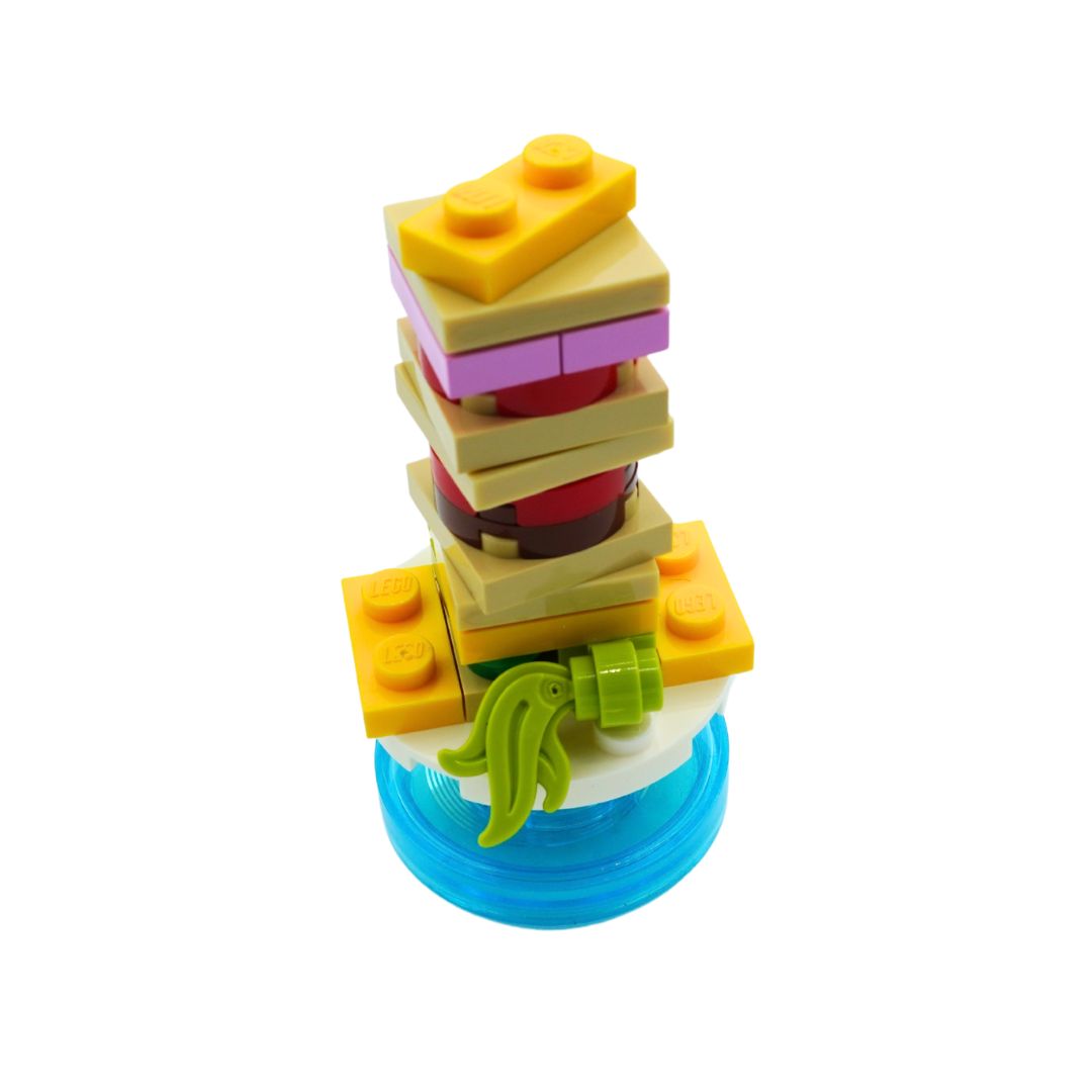 A small toy food tower or sandwich-style stack made from interlocking building blocks, including yellow, beige, purple, red, green, and blue pieces, isolated on a white background.