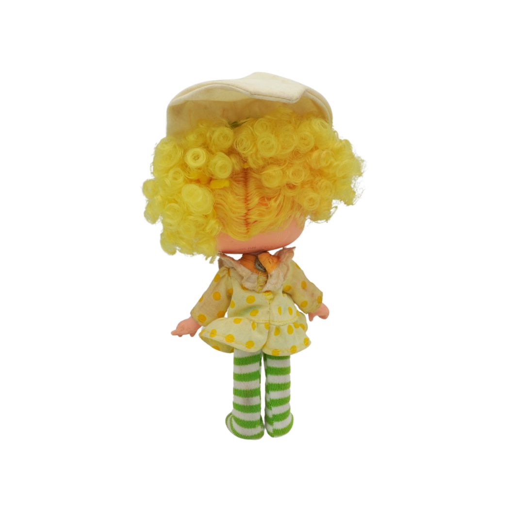 Small doll with yellow hair, dress, and shoes on a white background