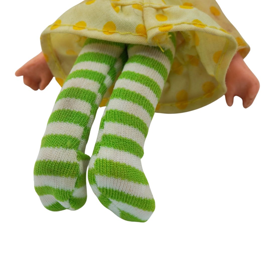 Doll with green and white striped socks and a yellow polka dot dress on a white background