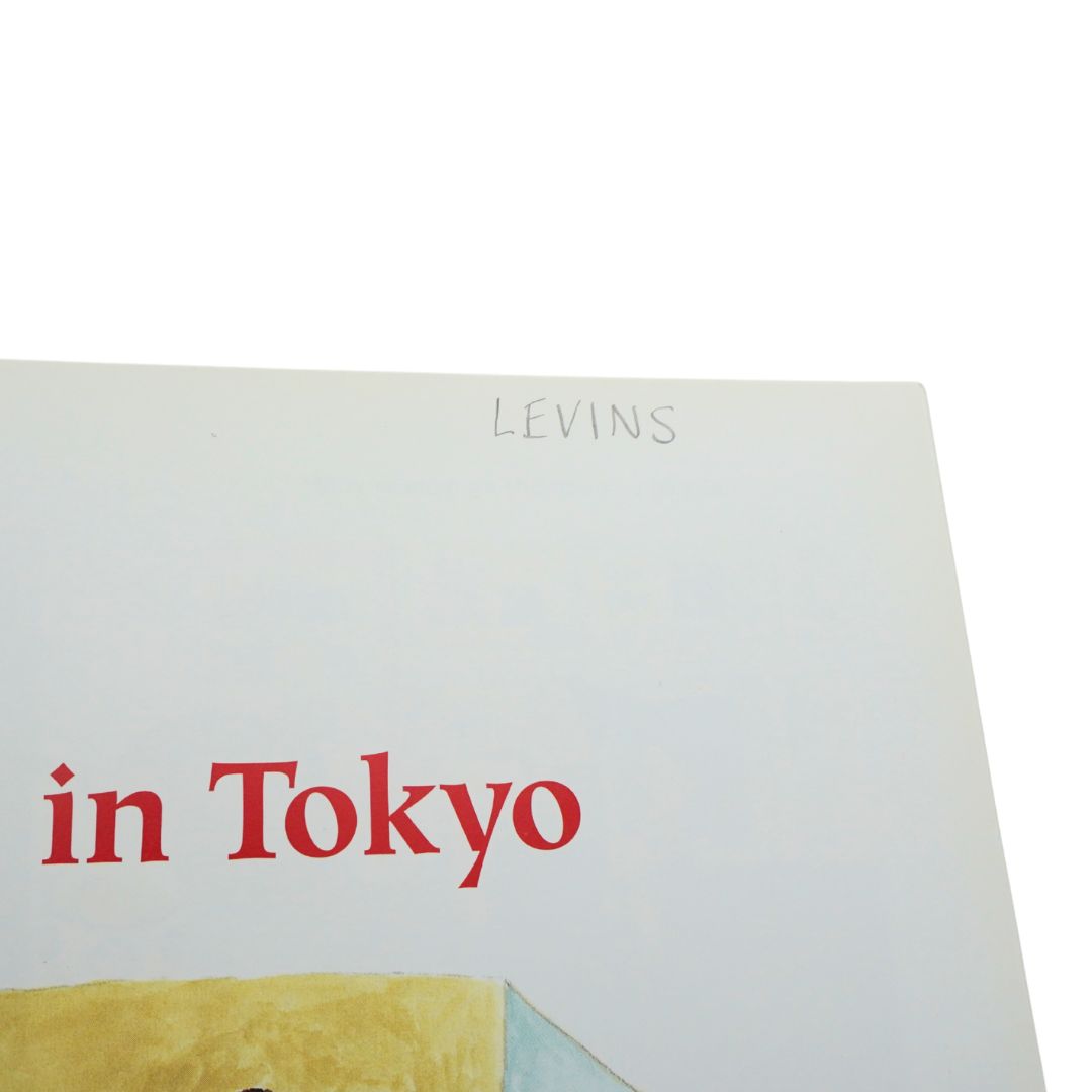 A close-up corner of a white art print or book cover with the word 'LEVINS' printed in gray at the top and 'in Tokyo' in large red serif text below. A small abstract yellow and pale blue shape appears at the bottom edge.